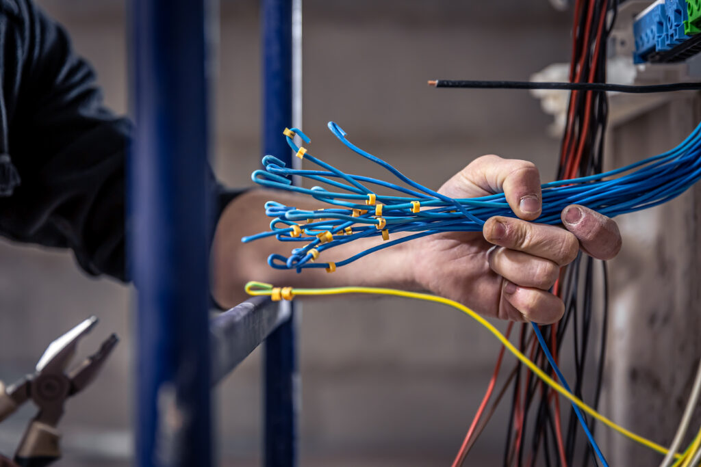 male electrician works in a switchboard with an electrical connecting cable